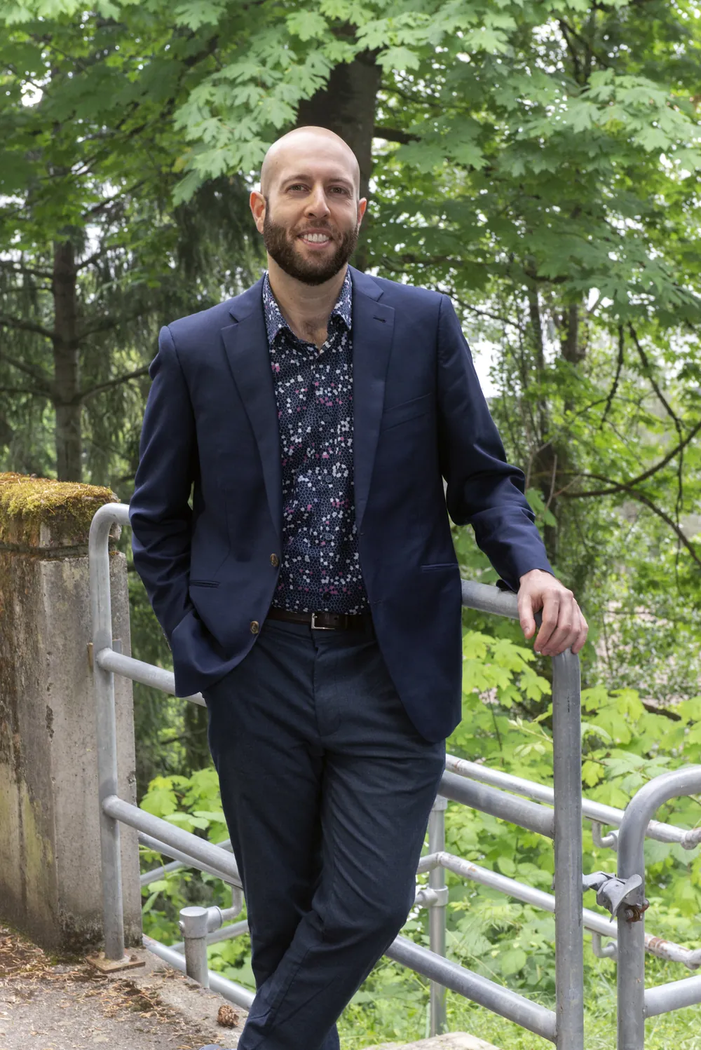 Dr. Aryan Sarparast in a navy suit, leaning on a railing among trees