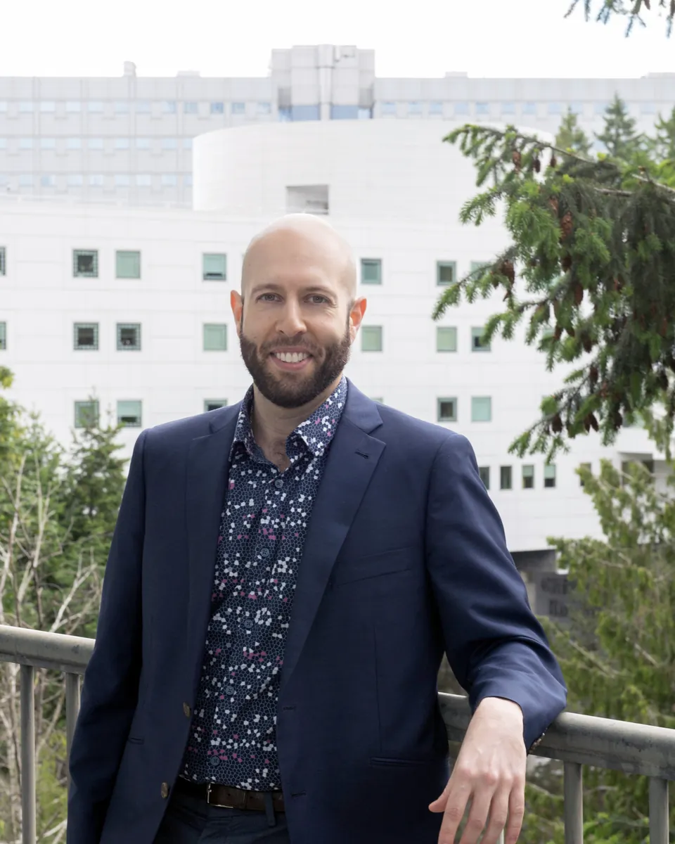 Dr. Aryan Sarparast in a navy blazer, leaning on a railing in front of an OHSU building